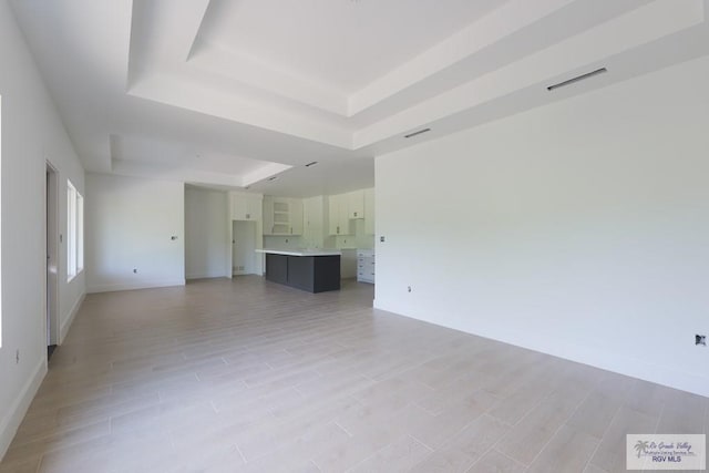 8830 Wentz Lk, Brownsville, TX 78520 - unfurnished living room featuring a tray ceiling, baseboards, and light wood-type flooring