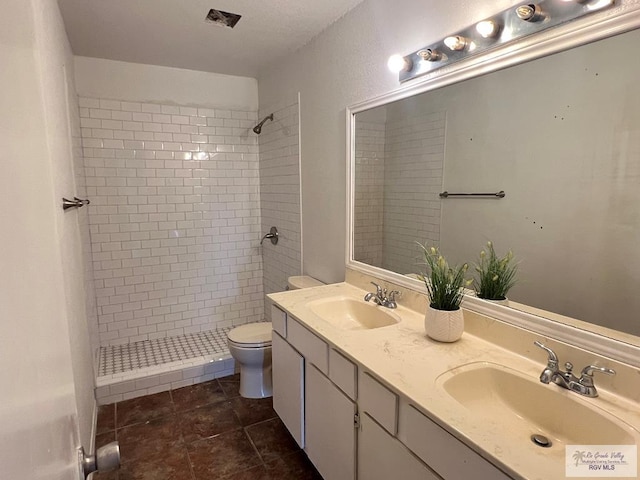 bathroom with tile patterned flooring, vanity, toilet, and tiled shower