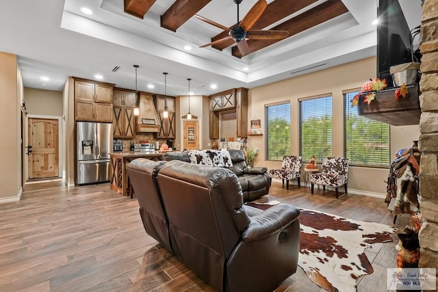 living room with ceiling fan, a raised ceiling, and light wood-type flooring