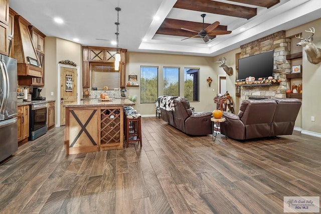 living room with dark hardwood / wood-style flooring, a tray ceiling, a stone fireplace, and ceiling fan