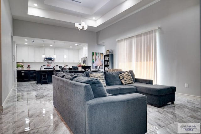 living room with baseboards, a tray ceiling, a high ceiling, marble finish floor, and a chandelier