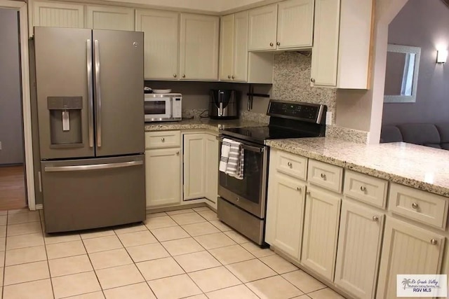 kitchen featuring light stone countertops, backsplash, stainless steel appliances, light tile patterned floors, and cream cabinets