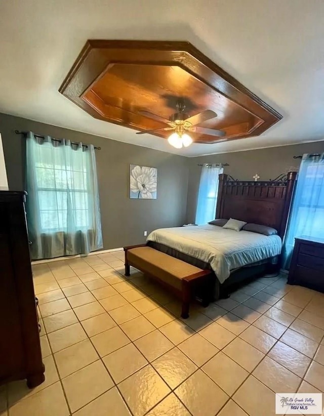 tiled bedroom featuring ceiling fan, multiple windows, and a tray ceiling