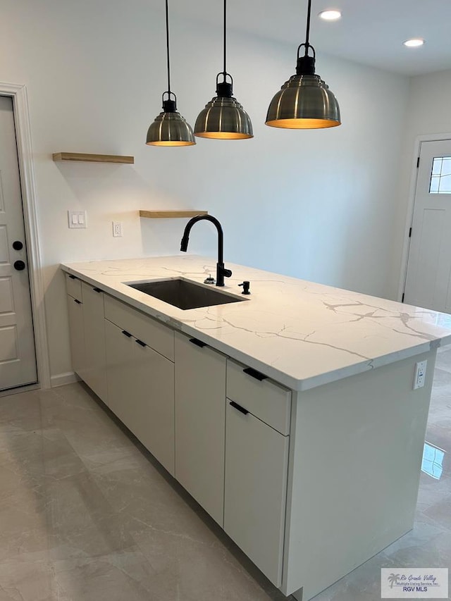 kitchen with light stone counters, sink, and decorative light fixtures