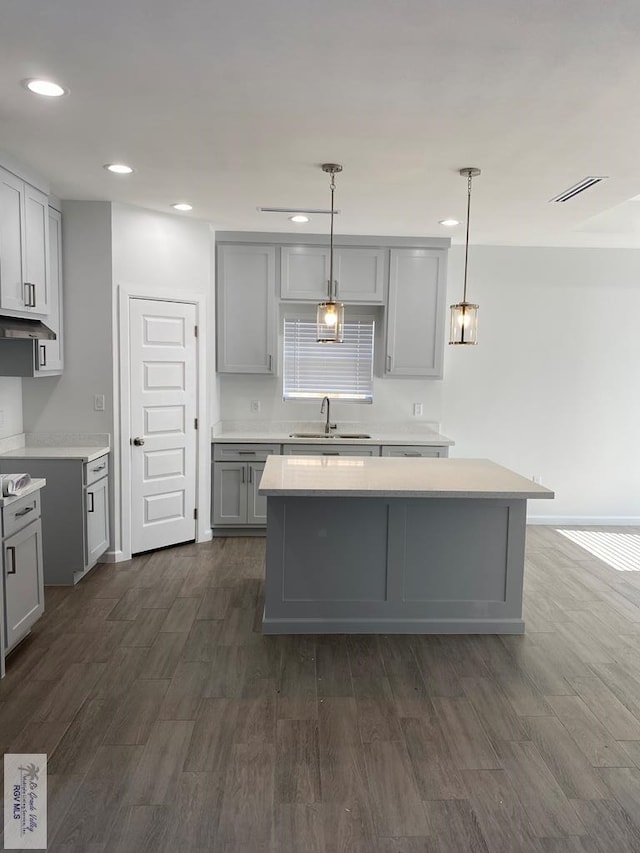 kitchen with dark hardwood / wood-style flooring, gray cabinetry, sink, a kitchen island, and hanging light fixtures