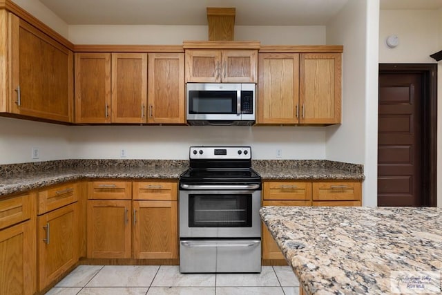 6705 Stone Oak Dr, Brownsville, TX 78526 - kitchen with stainless steel appliances, light tile patterned flooring, brown cabinetry, and dark stone counters