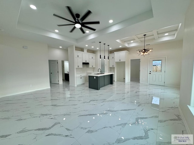 kitchen with pendant lighting, a kitchen island with sink, coffered ceiling, sink, and white cabinetry