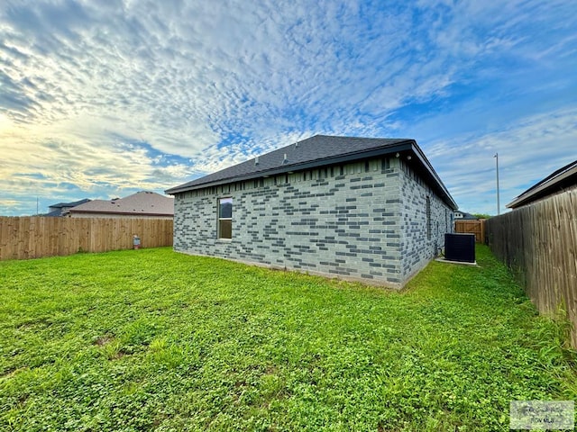 view of home's exterior featuring a lawn, central AC, a fenced backyard, and brick siding