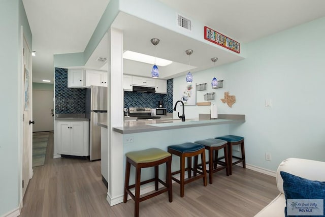 kitchen featuring white cabinets, stainless steel appliances, kitchen peninsula, and hanging light fixtures