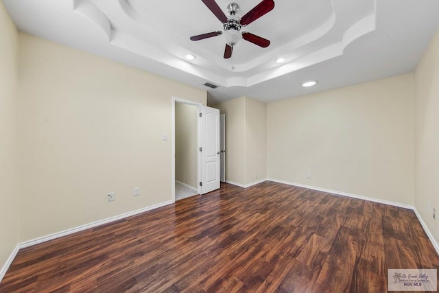 unfurnished bedroom featuring a tray ceiling, ceiling fan, and dark hardwood / wood-style flooring