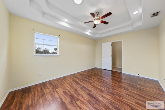 spare room featuring a raised ceiling, ceiling fan, and dark hardwood / wood-style floors