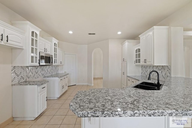 3271 Emerald Valley Blvd Unit 8, Brownsville, TX 78526 - kitchen featuring stainless steel microwave, a peninsula, light stone counters, light tile patterned floors, and glass insert cabinets
