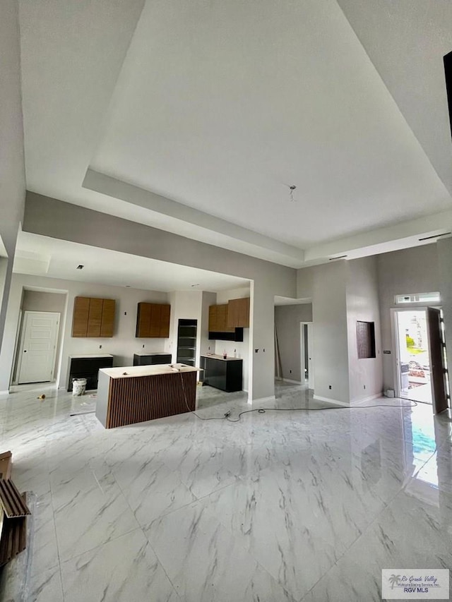 unfurnished living room featuring marble finish floor, baseboards, and a tray ceiling