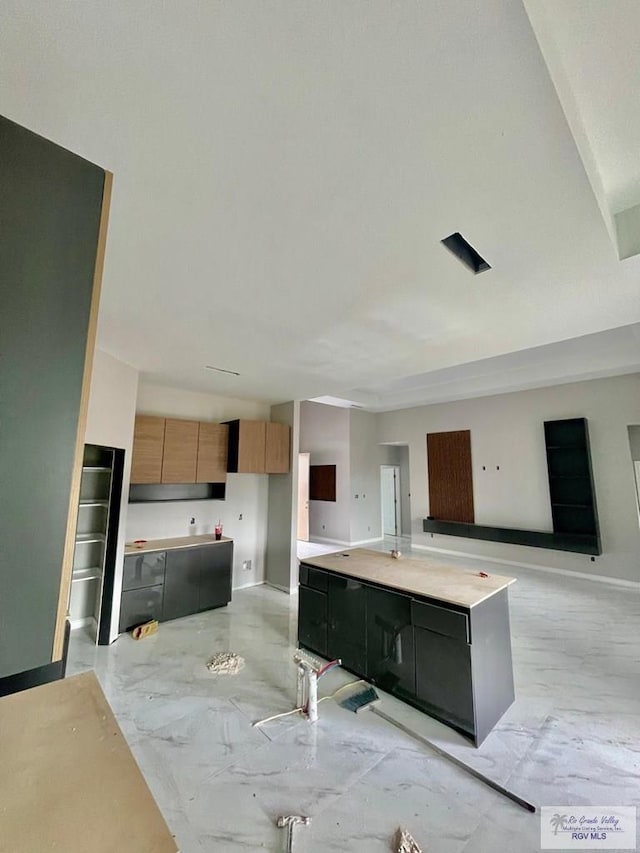 kitchen with marble finish floor, a kitchen island, open floor plan, light countertops, and baseboards