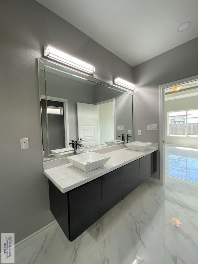 full bath featuring double vanity, marble finish floor, and a sink