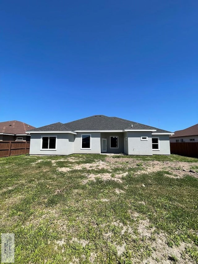 rear view of house with stucco siding, a lawn, and fence