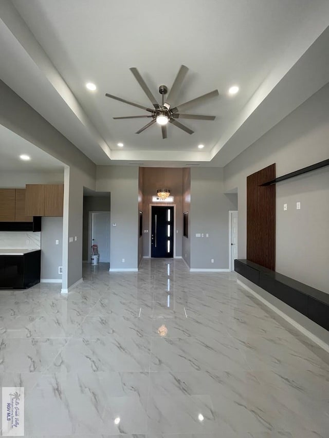 unfurnished living room featuring recessed lighting, a tray ceiling, baseboards, and a ceiling fan