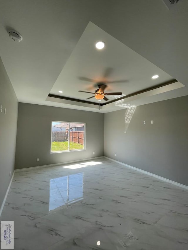 spare room featuring marble finish floor, a raised ceiling, baseboards, and ceiling fan