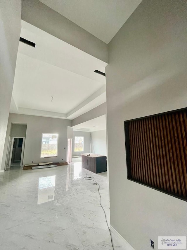 unfurnished living room featuring baseboards, a raised ceiling, and marble finish floor