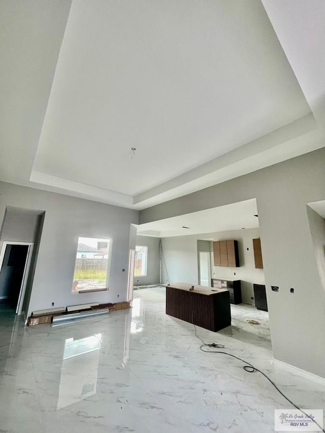 unfurnished living room featuring a tray ceiling, baseboards, and marble finish floor