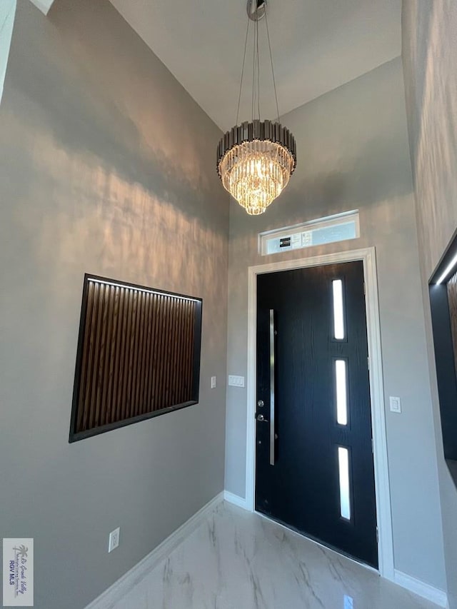 entryway with an inviting chandelier, baseboards, and marble finish floor