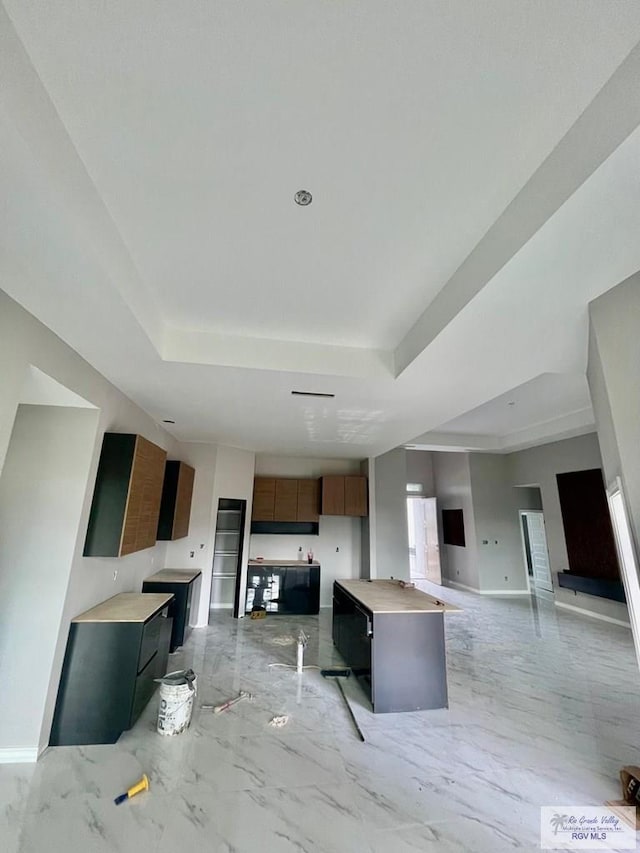 kitchen featuring open floor plan, marble finish floor, a raised ceiling, and baseboards