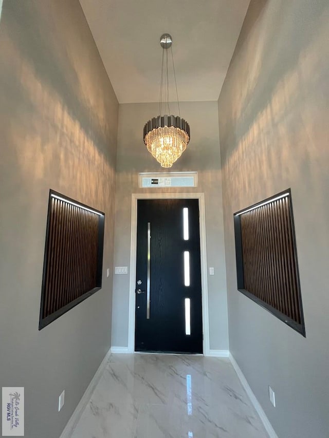 foyer featuring marble finish floor, an inviting chandelier, and baseboards