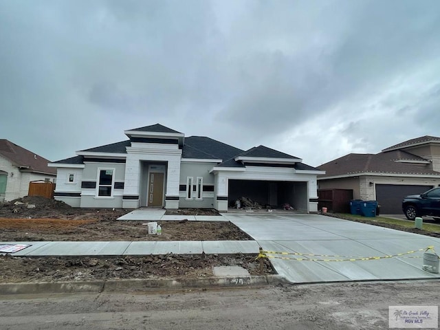 prairie-style home featuring a garage, a shingled roof, driveway, and stucco siding