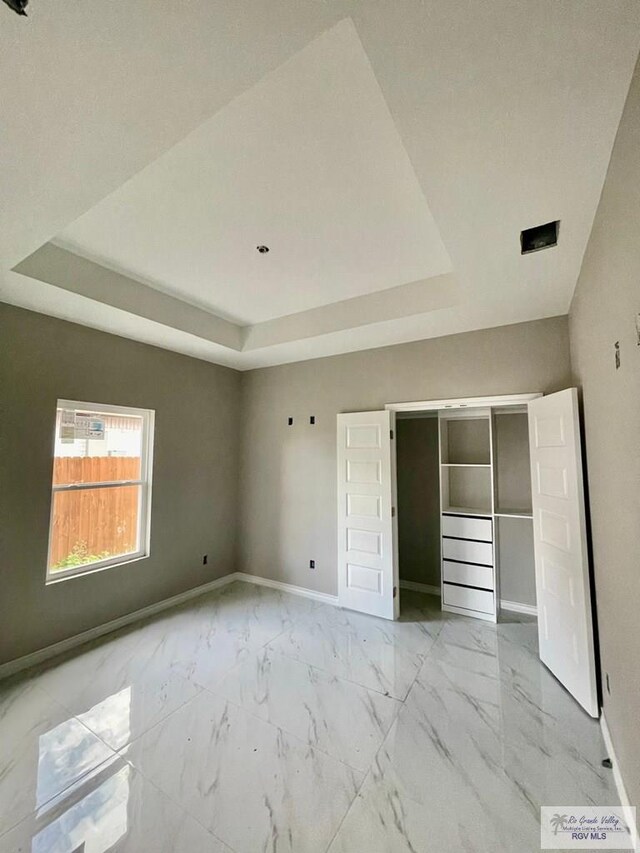 unfurnished bedroom featuring marble finish floor, baseboards, and a tray ceiling