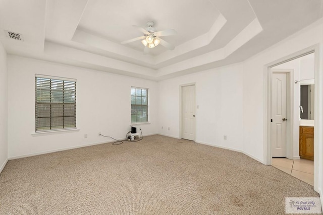 spare room featuring light colored carpet, a raised ceiling, ceiling fan, and a healthy amount of sunlight