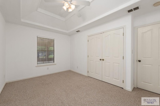 unfurnished bedroom featuring ceiling fan, a raised ceiling, light carpet, and a closet