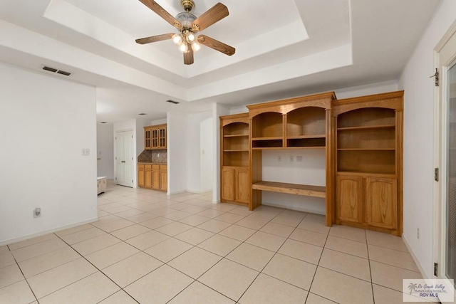 unfurnished living room featuring a raised ceiling, ceiling fan, and light tile patterned flooring