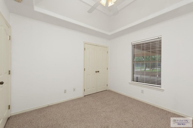 carpeted empty room featuring a tray ceiling and ceiling fan