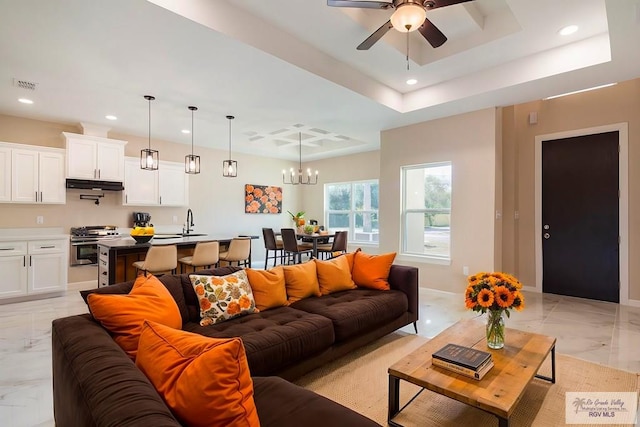 living room featuring ceiling fan with notable chandelier, a raised ceiling, and sink