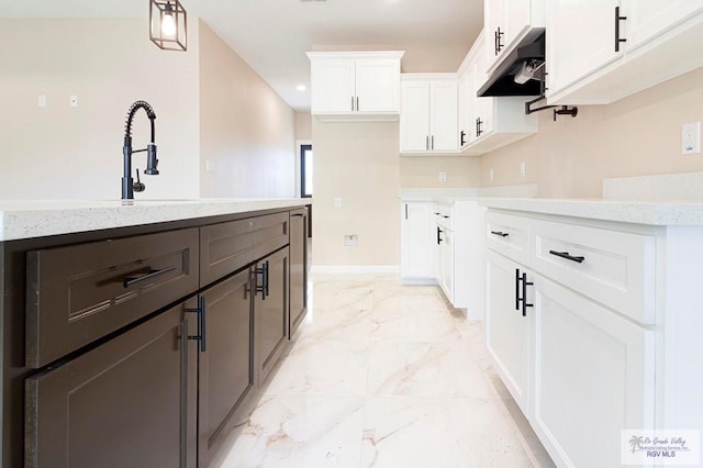 kitchen featuring white cabinetry, hanging light fixtures, light stone counters, and sink