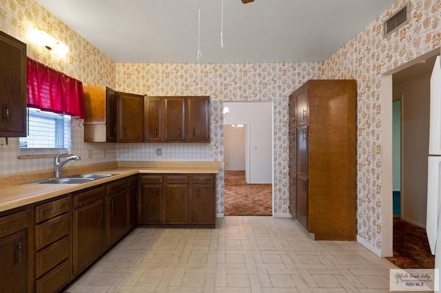 kitchen with light countertops, wallpapered walls, visible vents, and a sink