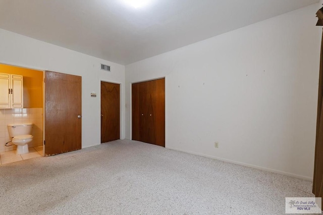 unfurnished bedroom with two closets, visible vents, light colored carpet, and connected bathroom