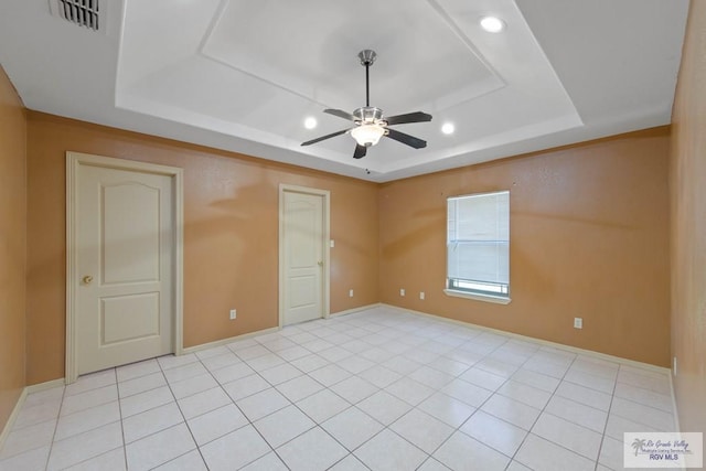 unfurnished bedroom with light tile patterned floors, a ceiling fan, visible vents, baseboards, and a tray ceiling