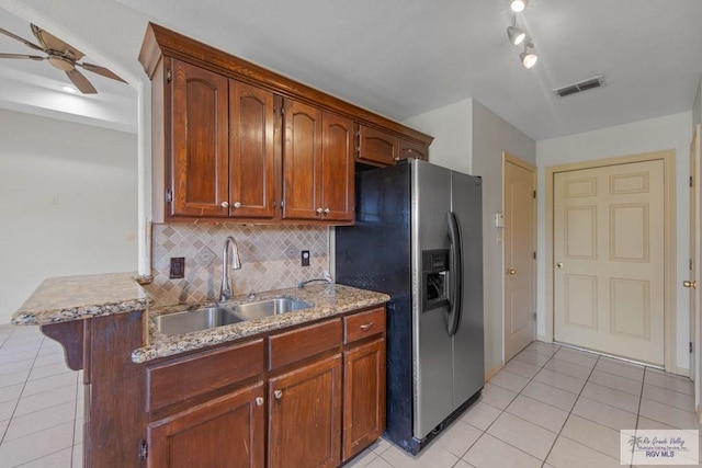 kitchen with light tile patterned floors, brown cabinetry, a sink, a peninsula, and stainless steel fridge with ice dispenser