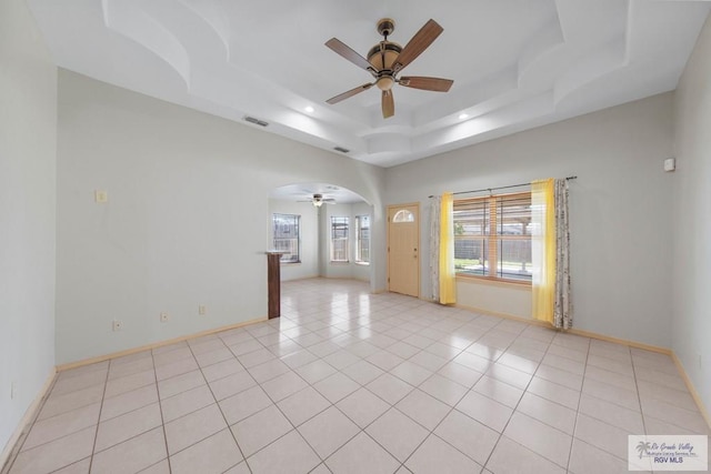 spare room with arched walkways, light tile patterned floors, visible vents, baseboards, and a raised ceiling