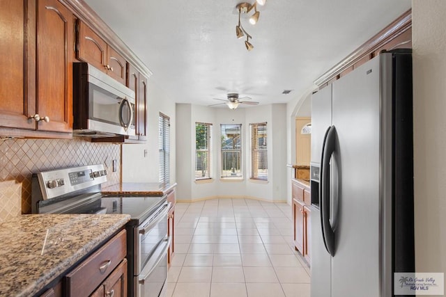 kitchen featuring light tile patterned floors, tasteful backsplash, appliances with stainless steel finishes, brown cabinetry, and a ceiling fan