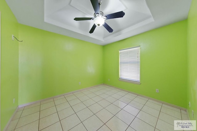 empty room with a raised ceiling, ceiling fan, baseboards, and light tile patterned floors