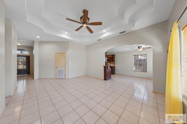 spare room featuring arched walkways, a raised ceiling, visible vents, and light tile patterned floors