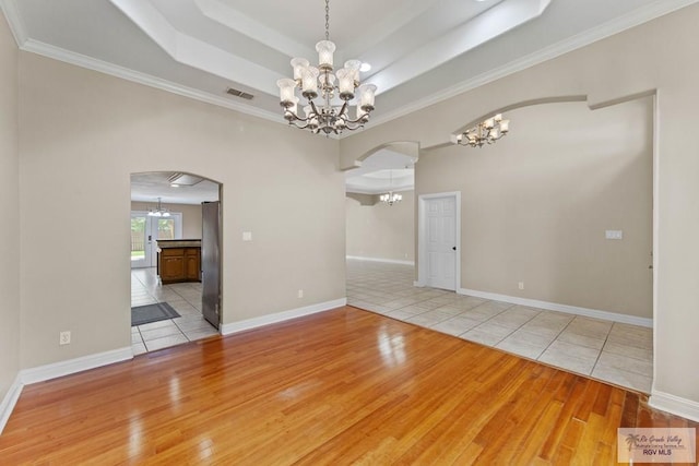 empty room featuring a notable chandelier, light wood-type flooring, and crown molding