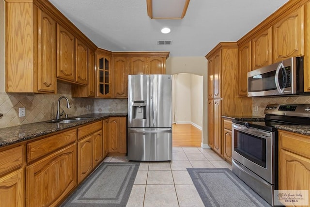 kitchen with backsplash, sink, dark stone countertops, light tile patterned floors, and appliances with stainless steel finishes