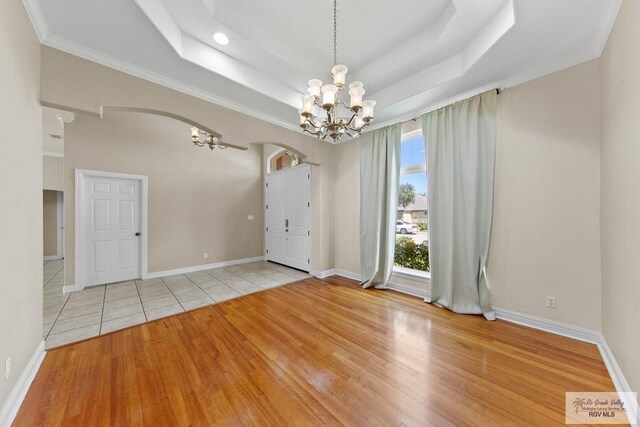 unfurnished room with a raised ceiling, light wood-type flooring, crown molding, and a chandelier