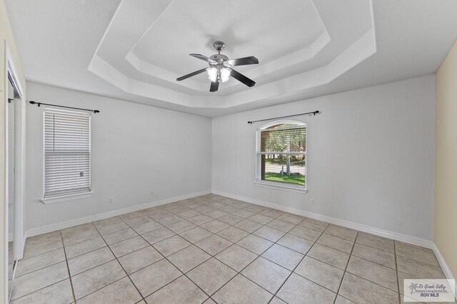 tiled spare room featuring a tray ceiling and ceiling fan