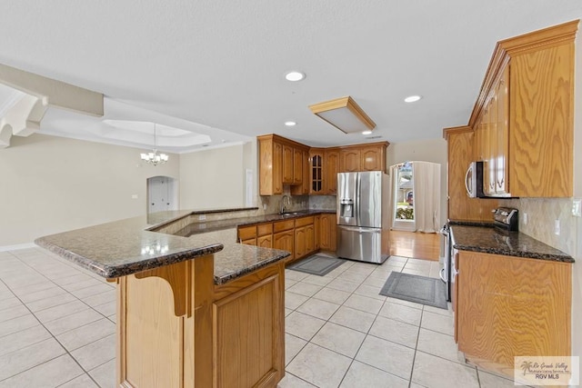 kitchen featuring kitchen peninsula, decorative backsplash, dark stone counters, stainless steel appliances, and light tile patterned floors