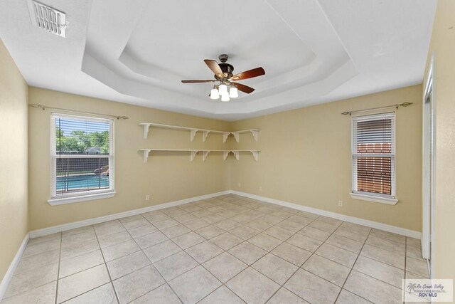 tiled empty room featuring a raised ceiling and ceiling fan