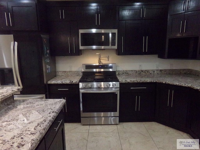 kitchen featuring dark brown cabinetry, stainless steel appliances, and light stone counters